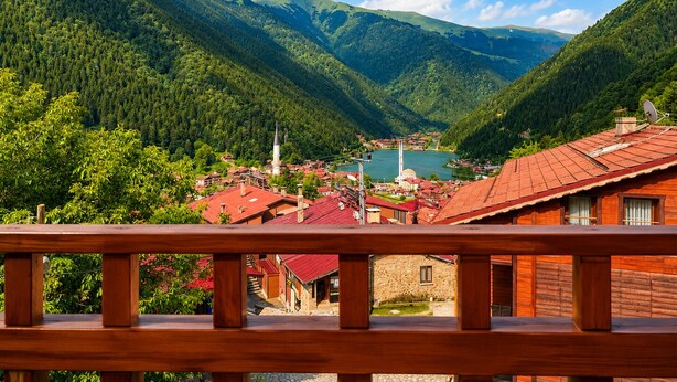 Un paisaje montañoso con un pueblo, edificios de techo rojo y una torre blanca destacada.