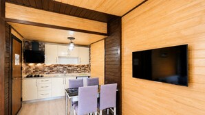 Una cocina compacta con paredes de madera, una zona de comedor con sillas y un televisor montado.