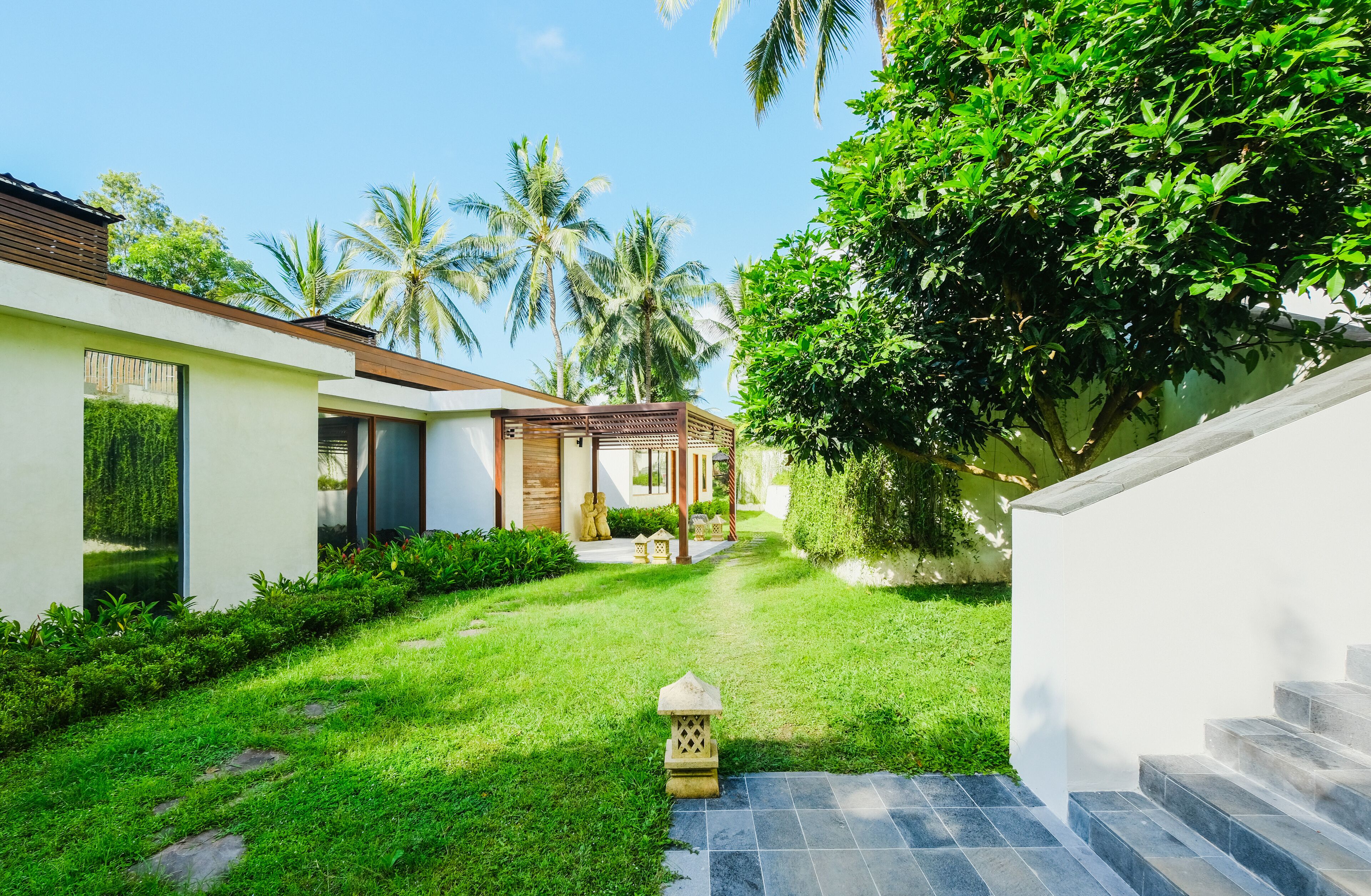 A modern villa with a well-maintained garden, palm trees, and a clear sky.