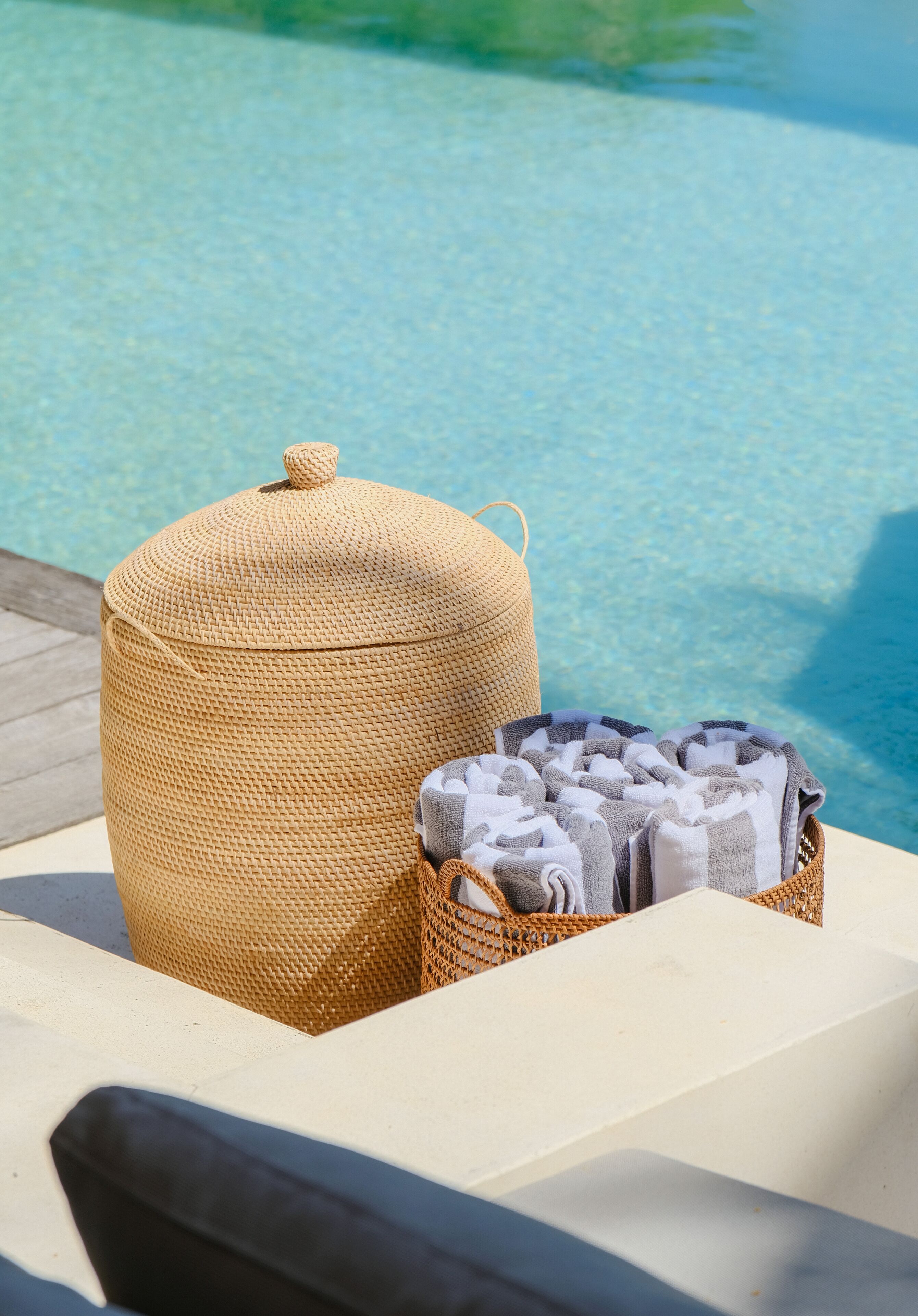 Zona junto a la piscina con una cesta tejida que contiene toallas y un taburete tejido.