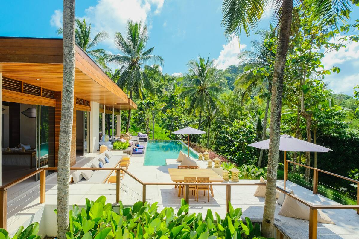 A modern house with a pool, surrounded by lush greenery and palm trees.