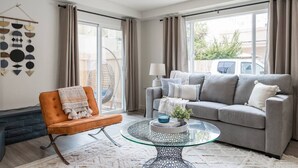 En moderne stue med en grå sofa, en orange lænestol og et glasbord.