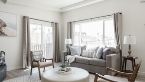 Una sala de estar moderna con un sofá gris, dos sillones, un otoman redondos y una mesita de noche con una lámpara.