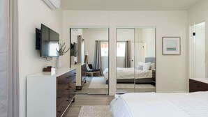 Un dormitorio moderno con cama, cómoda, televisor y espejo.