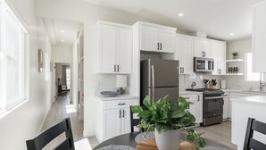 Una cocina moderna con armarios blancos, electrodomésticos de acero inoxidable y un comedor con una mesa redonda y sillas.