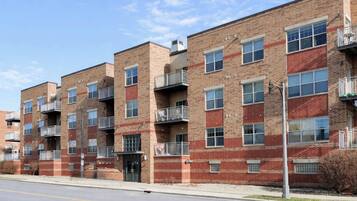 A multi-story brick building with balconies, a central entrance, and a clear sky.