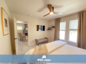 A bedroom with a bed, a ceiling fan, a TV, a bench, and a fireplace in the background.