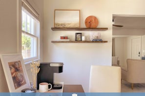 A cozy room with a coffee maker, framed picture, and a small shelf with books and a mug.