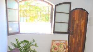 Een kamer met een bruine bank, een fauteuil met bloemenprint, een potplant en een houten deur.