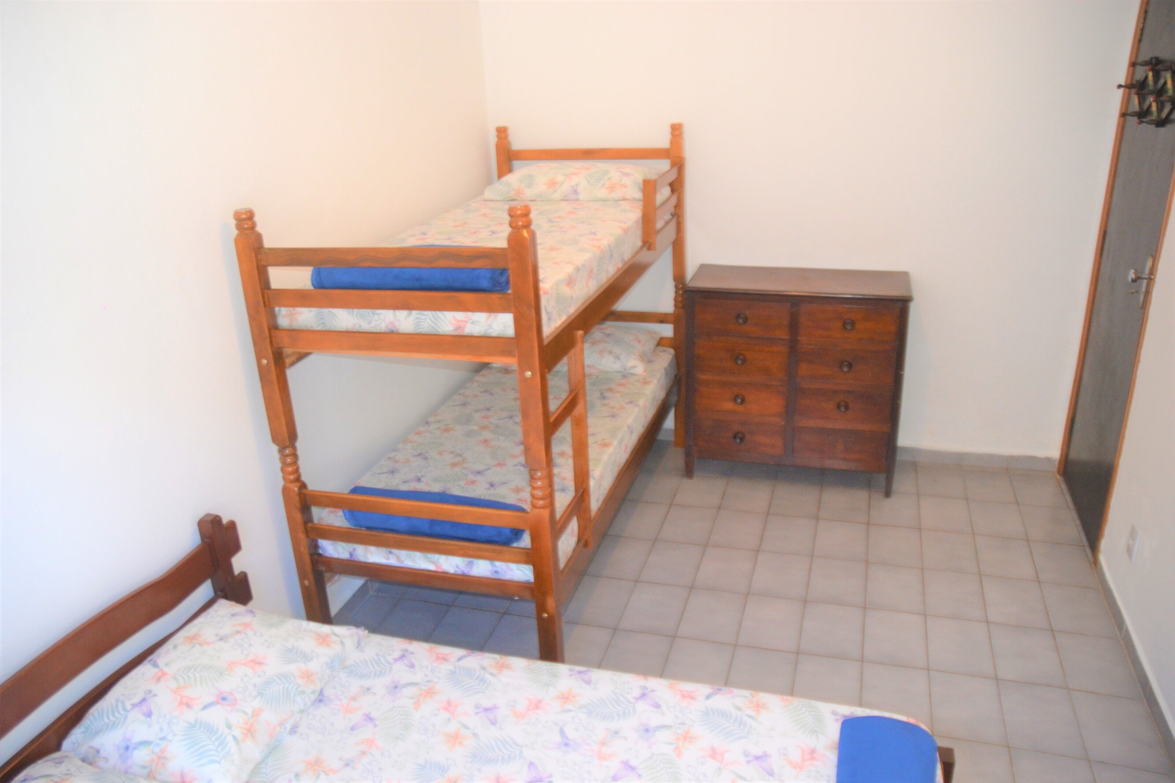 Una cama litera con un aparador de madera al lado en una habitación con suelo de baldosas.