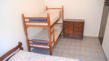 Una cama litera con un aparador de madera al lado en una habitación con suelo de baldosas.