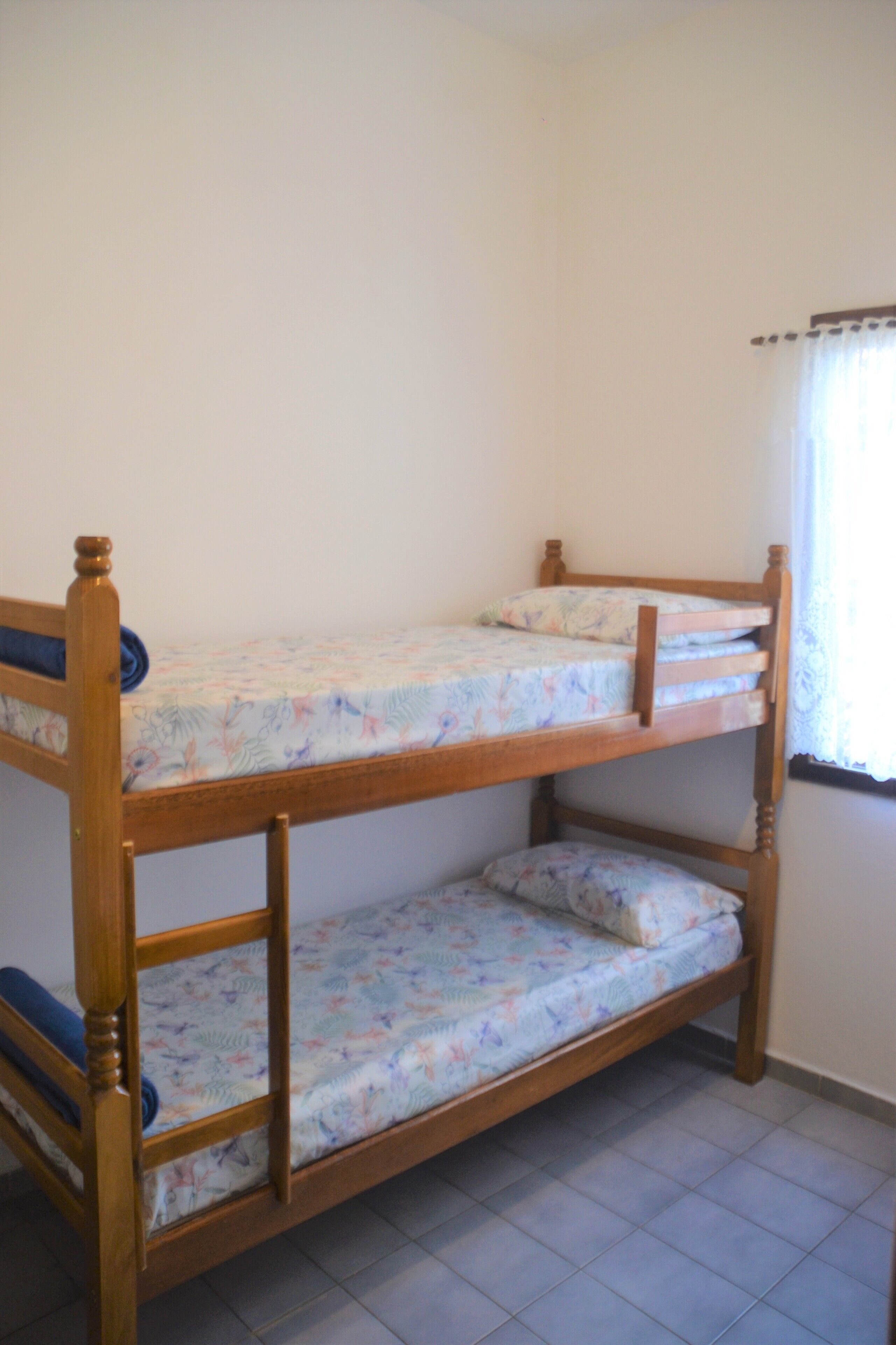 Una cama individual con ropa de cama floral en una habitación con paredes lisas y una ventana con cortinas.