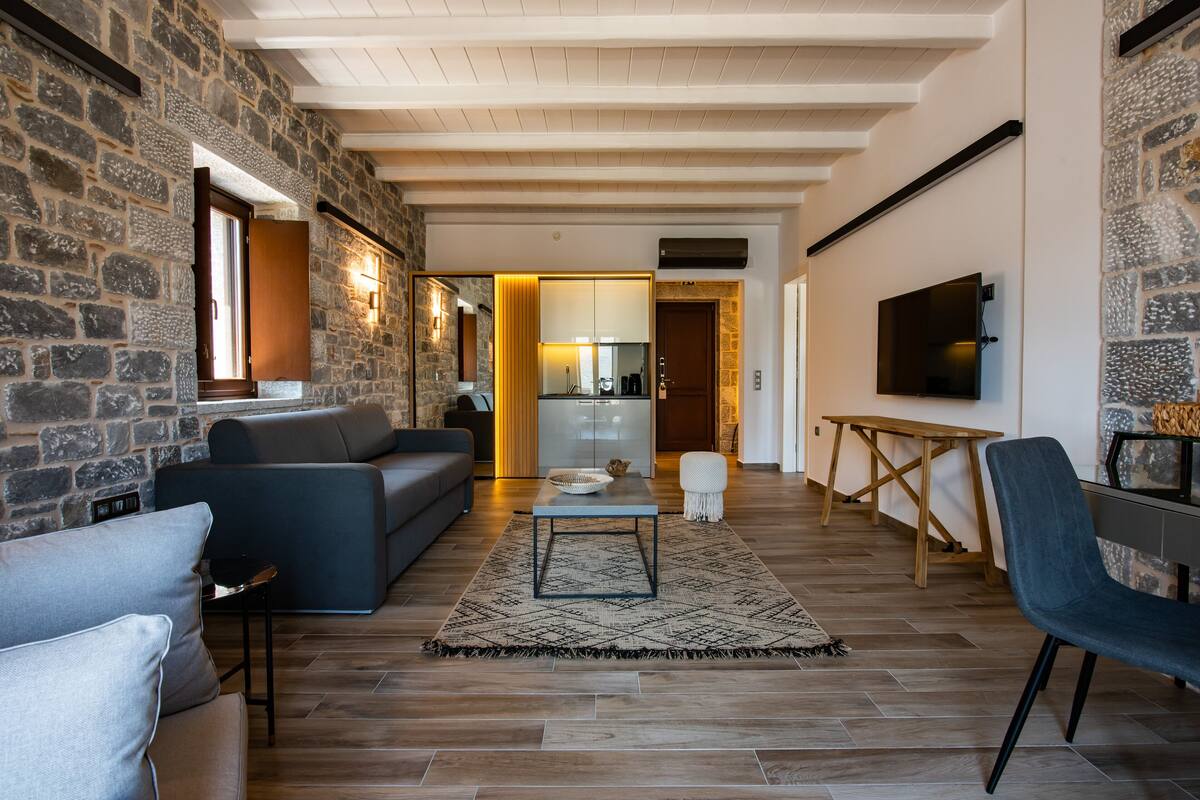 Ein modernes Wohnzimmer mit Steinwänden, einem grauen Sofa, einem Couchtisch und einem an der Wand montierten Fernseher.