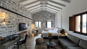 Ein modernes Schlafzimmer mit Steinwänden, einem großen Bett, einem Schreibtisch mit einem Laptop und Blick ins Freie durch Fenster.