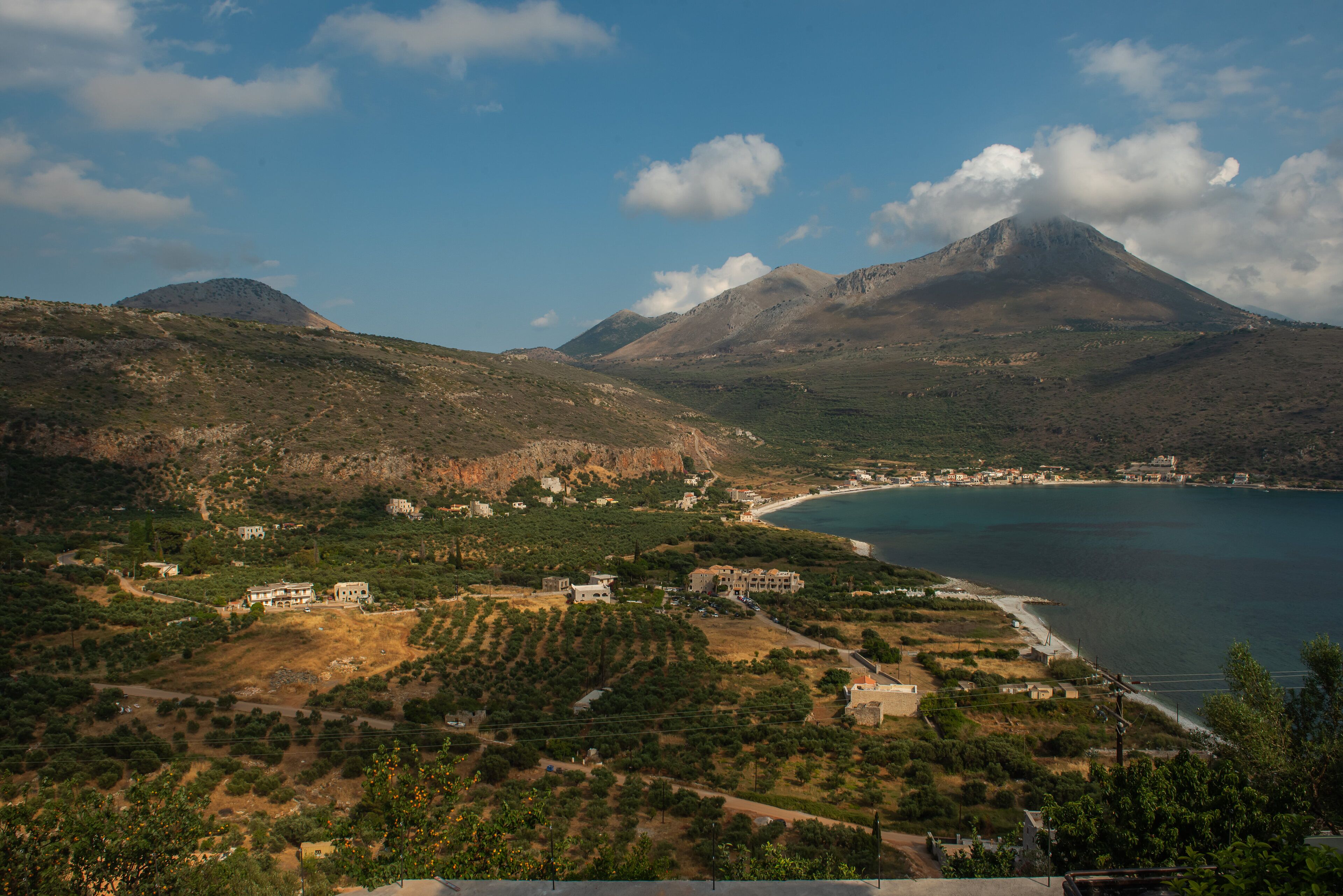 A coastal landscape with a mountain, a beach, and scattered buildings.