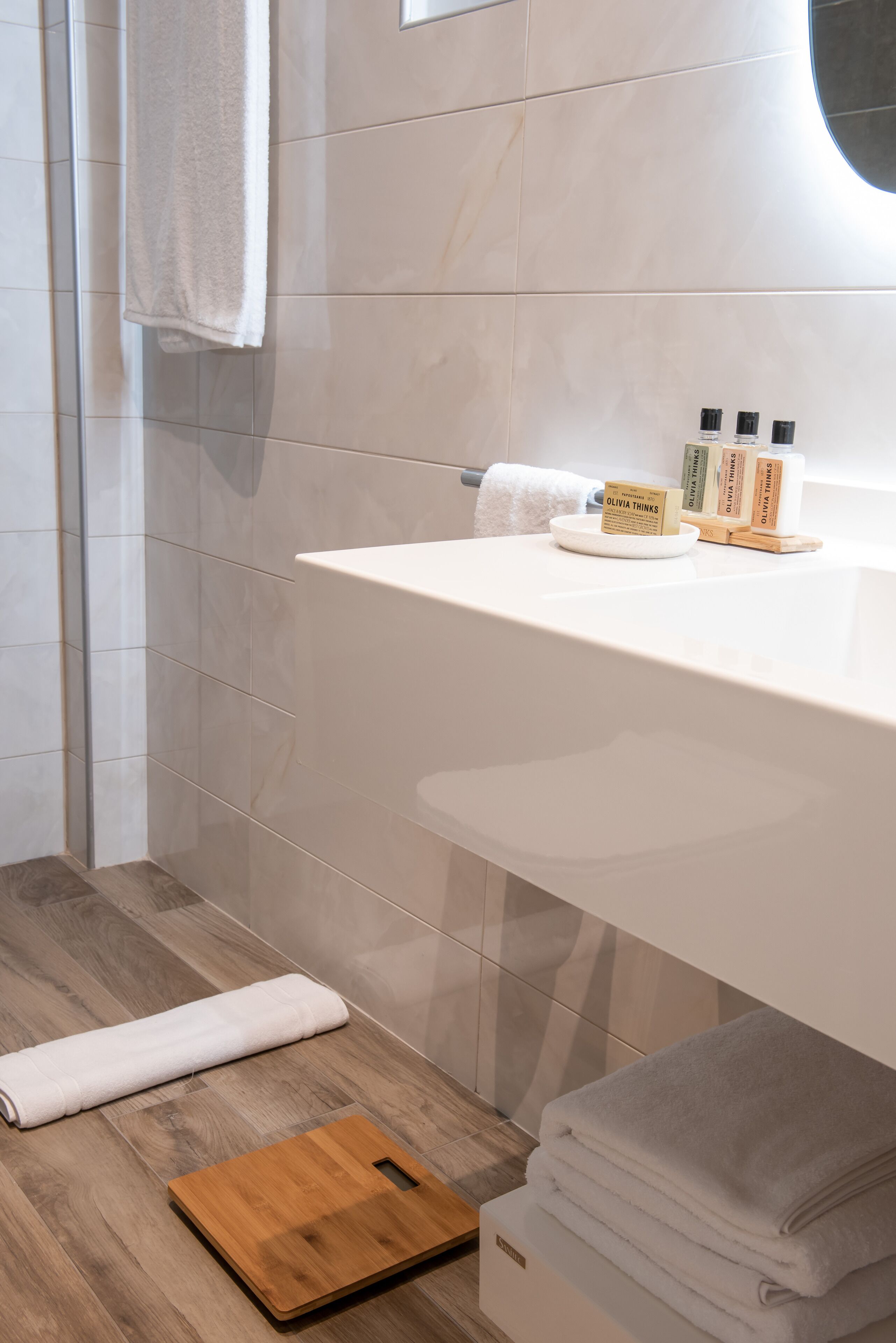 A modern bathroom with a white sink, toiletries, and a wooden cutting board on the floor.