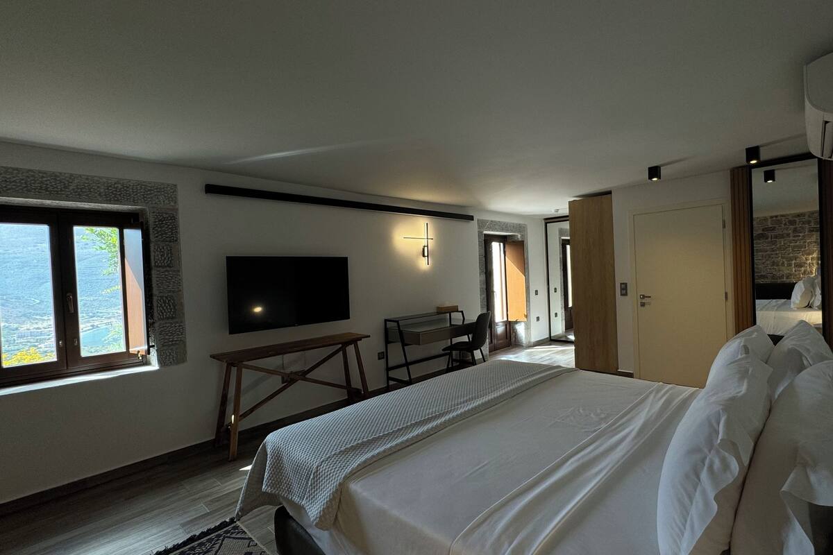 Ein Hotelzimmer mit einem großen Bett, einem Schreibtisch mit Stuhl, einem flachbildfernseher an der Wand und einem Fenster mit Blick ins Freie.