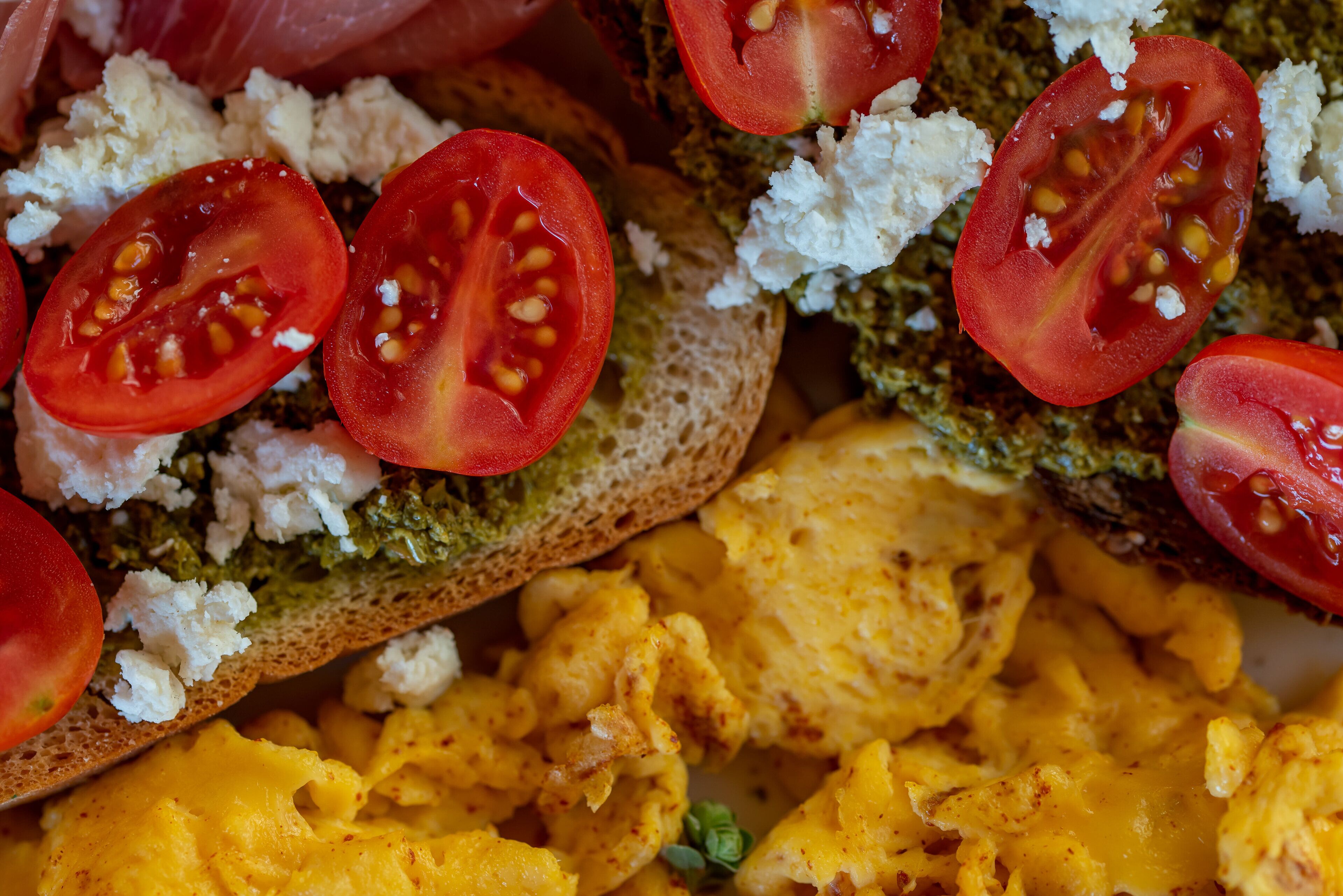 Gros plan d’un sandwich garni de tranches de tomates, de fromage et d’une pâte verte étalée sur du pain.