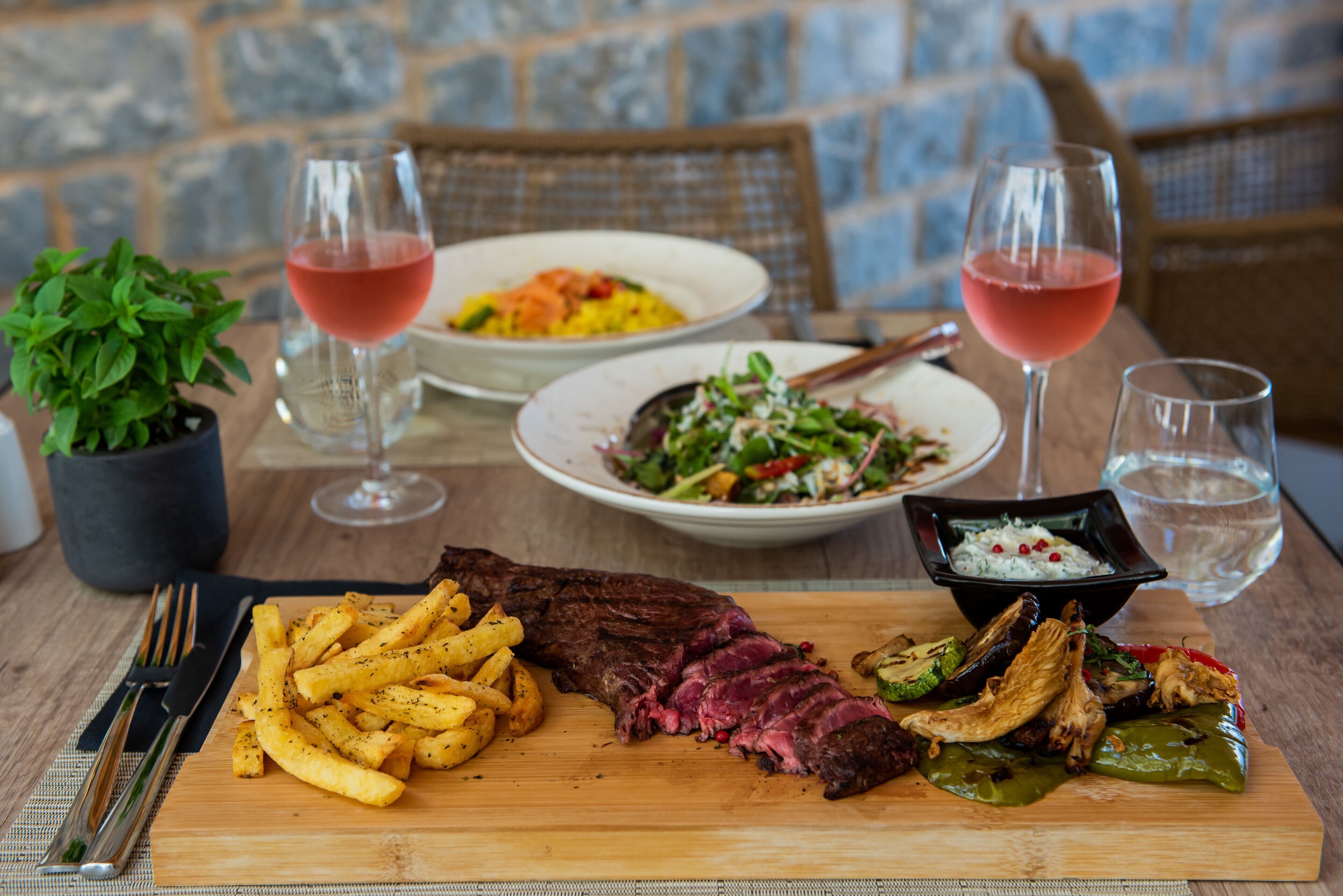 Une table en bois avec un steak, des frites et une salade, accompagnée de deux verres de vin rouge.