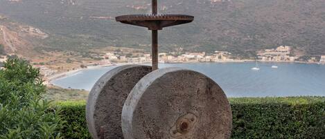 A stone sculpture with a cross on top, set on a stone platform with a view of a mountain and sea in the background.