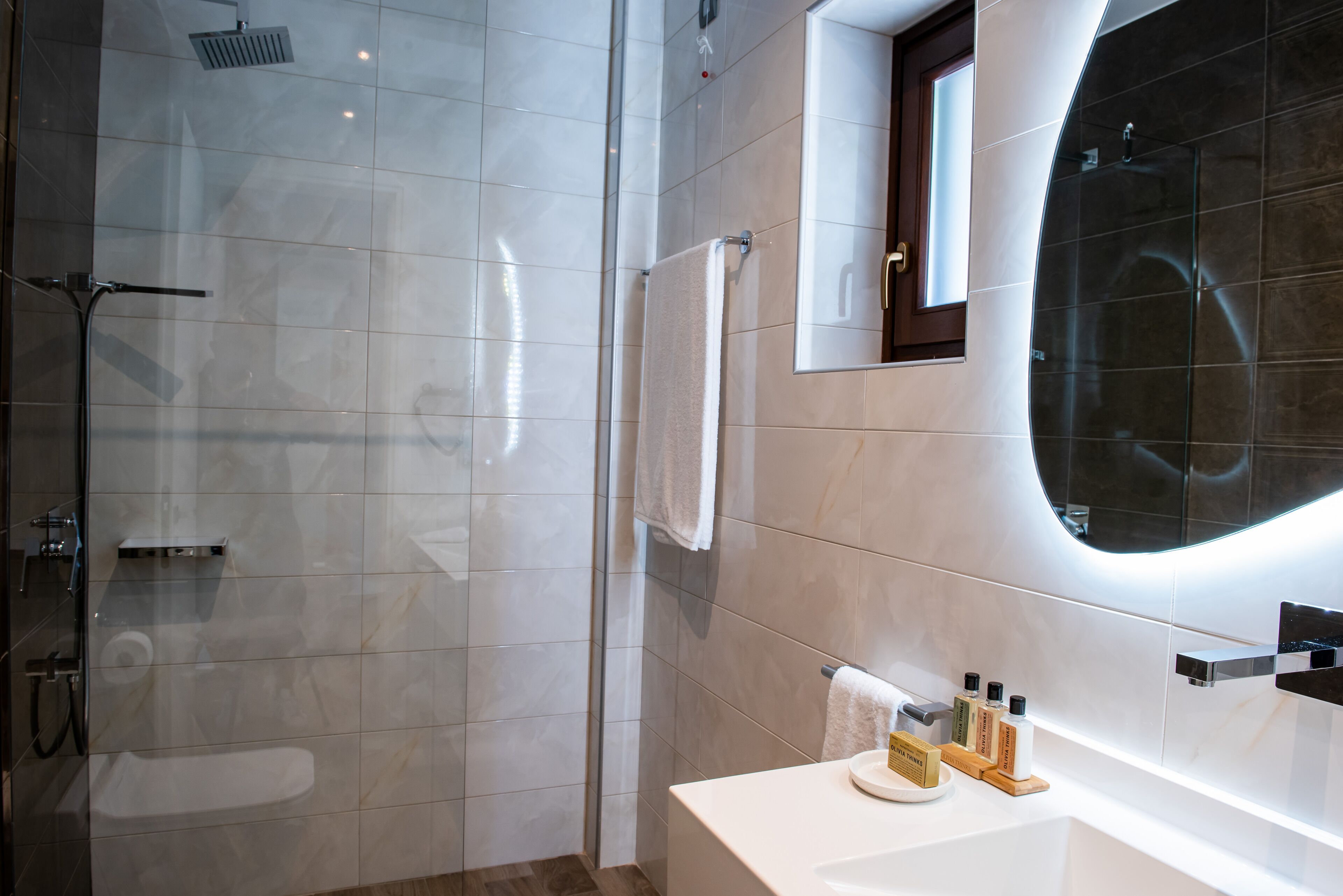 A modern bathroom with a glass-enclosed shower, a large mirror, and a white sink with toiletries.