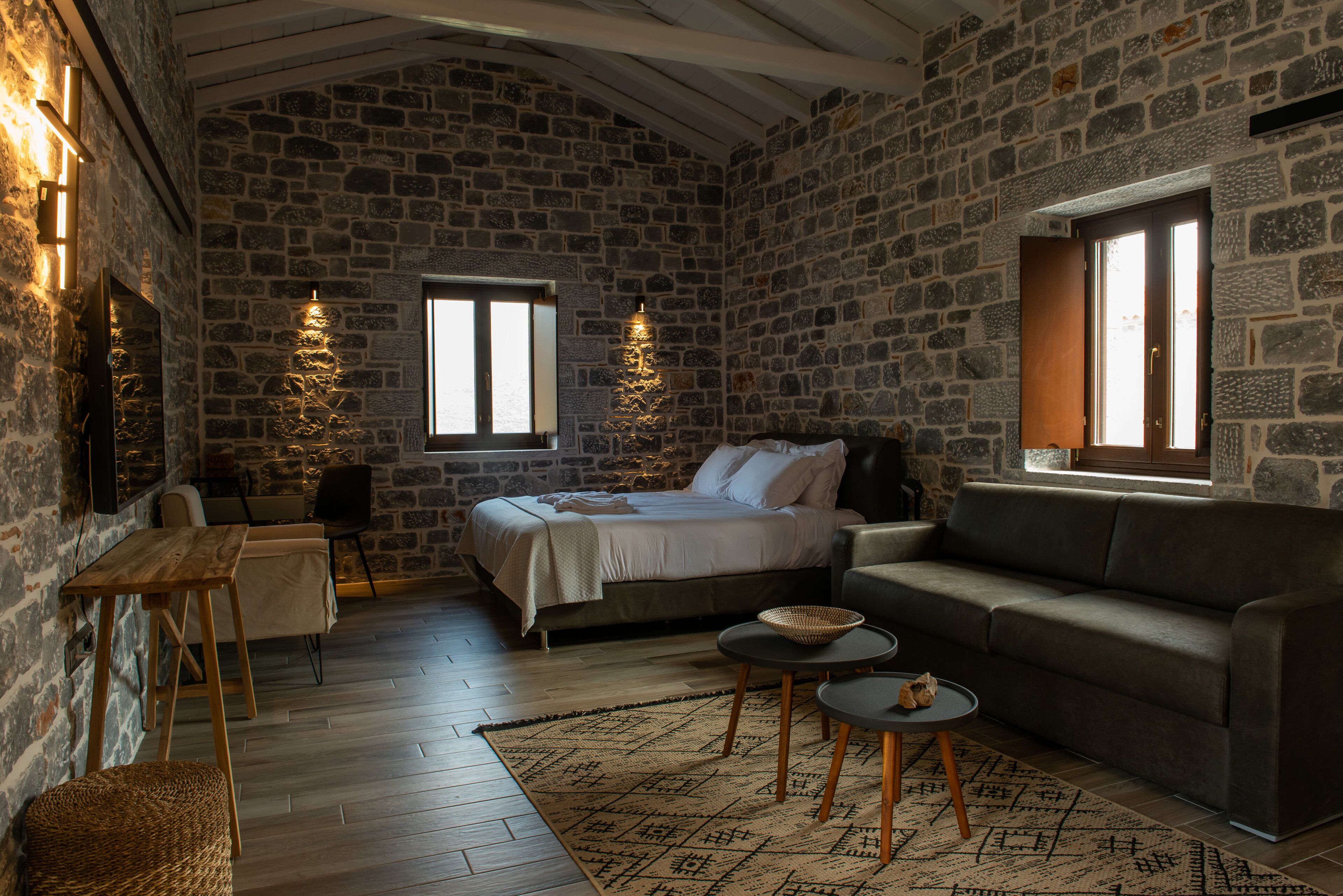 A cozy room with a stone wall, a bed, a sofa, a small table, and a window.