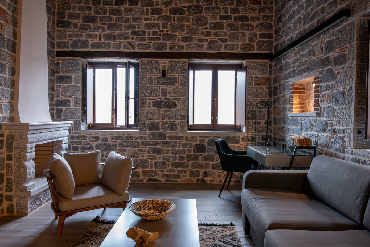 Ein Zimmer mit Stehwänden, einem Sofa, einem Sessel, einem Tisch und einem Kamin.