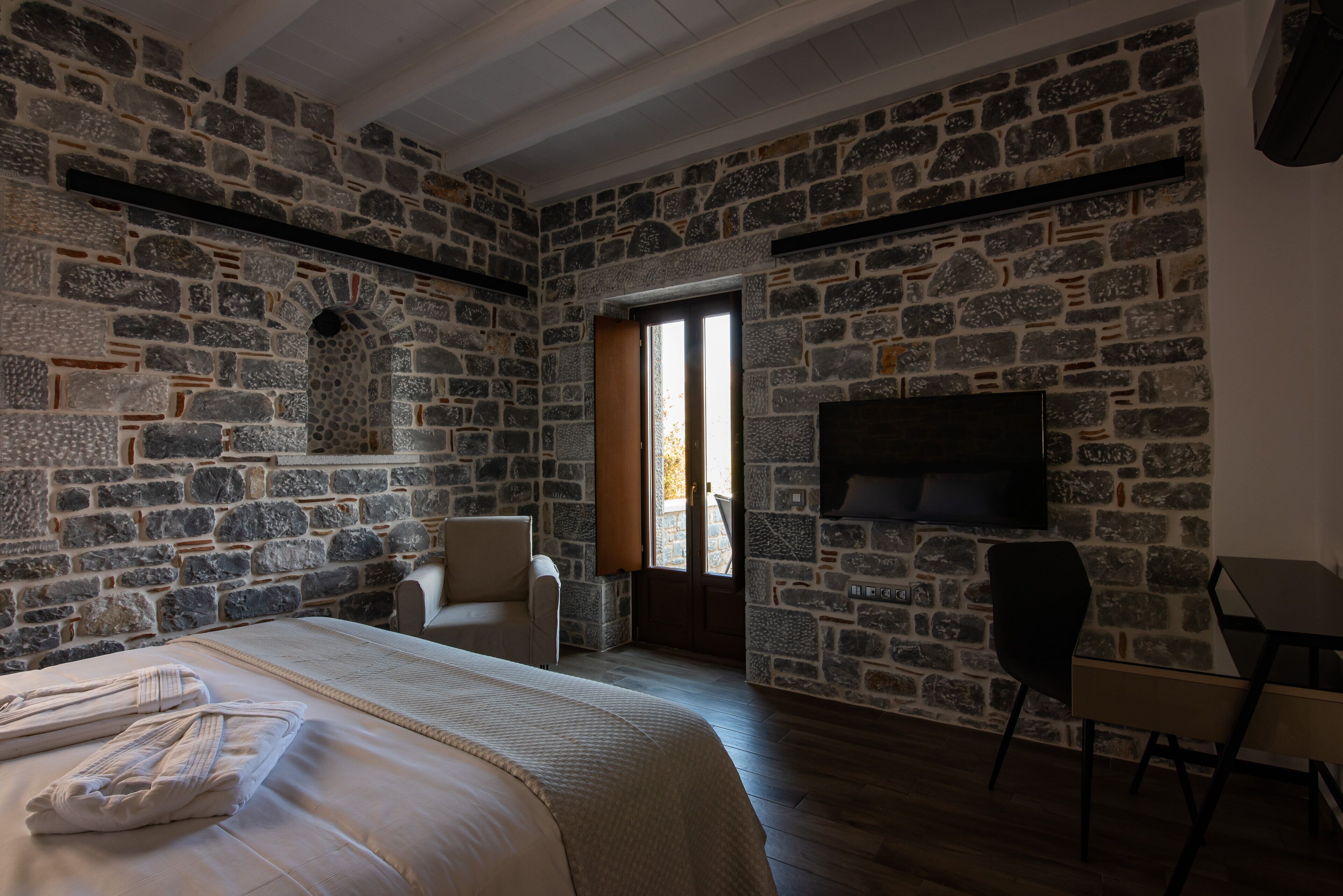 Una habitación con paredes de piedra, una cama con toallas, una silla, un escritorio y un televisor.