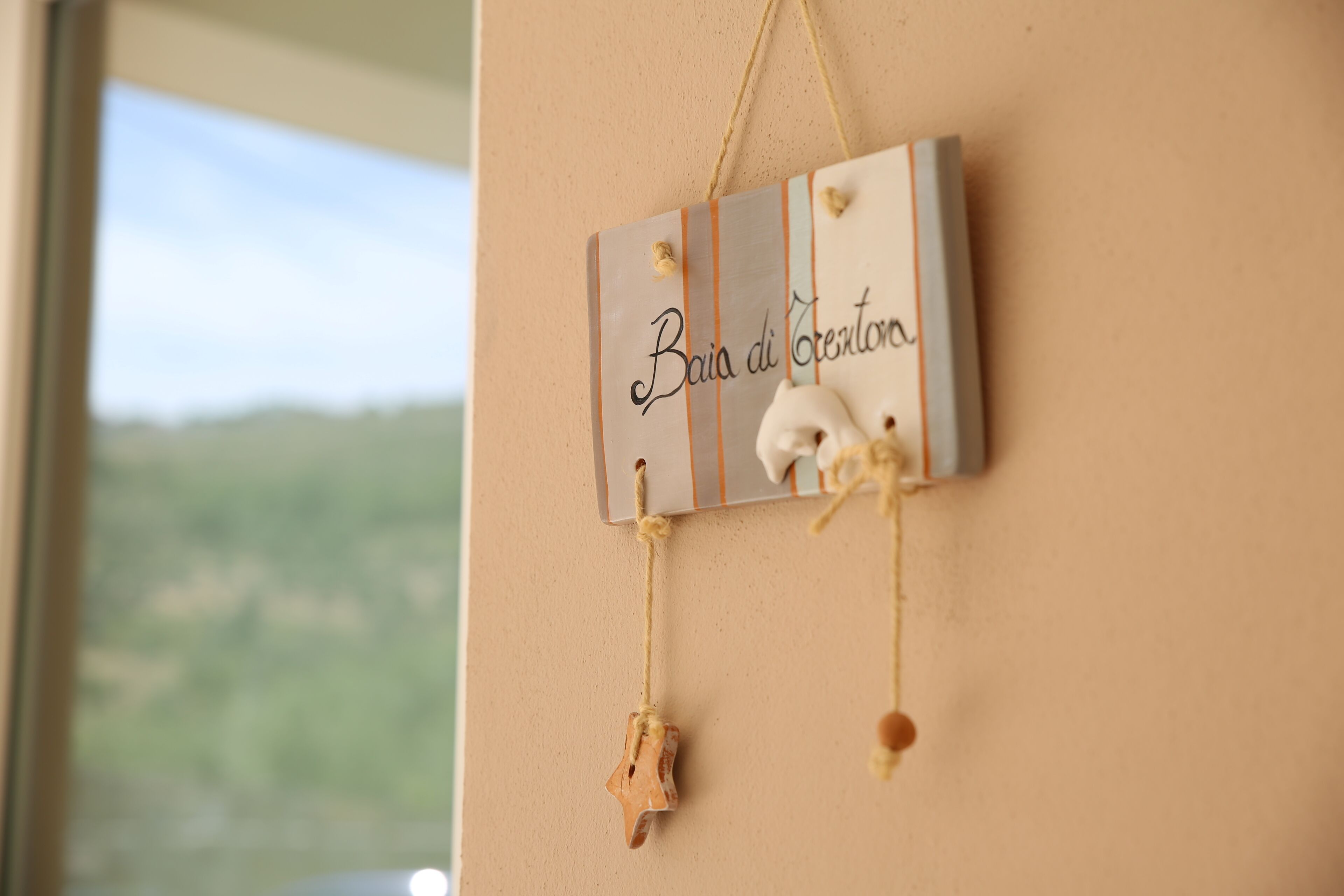 Une plaque fixée au mur, portant l’inscription « Baia di Creentora », et deux éléments décoratifs suspendus en dessous.