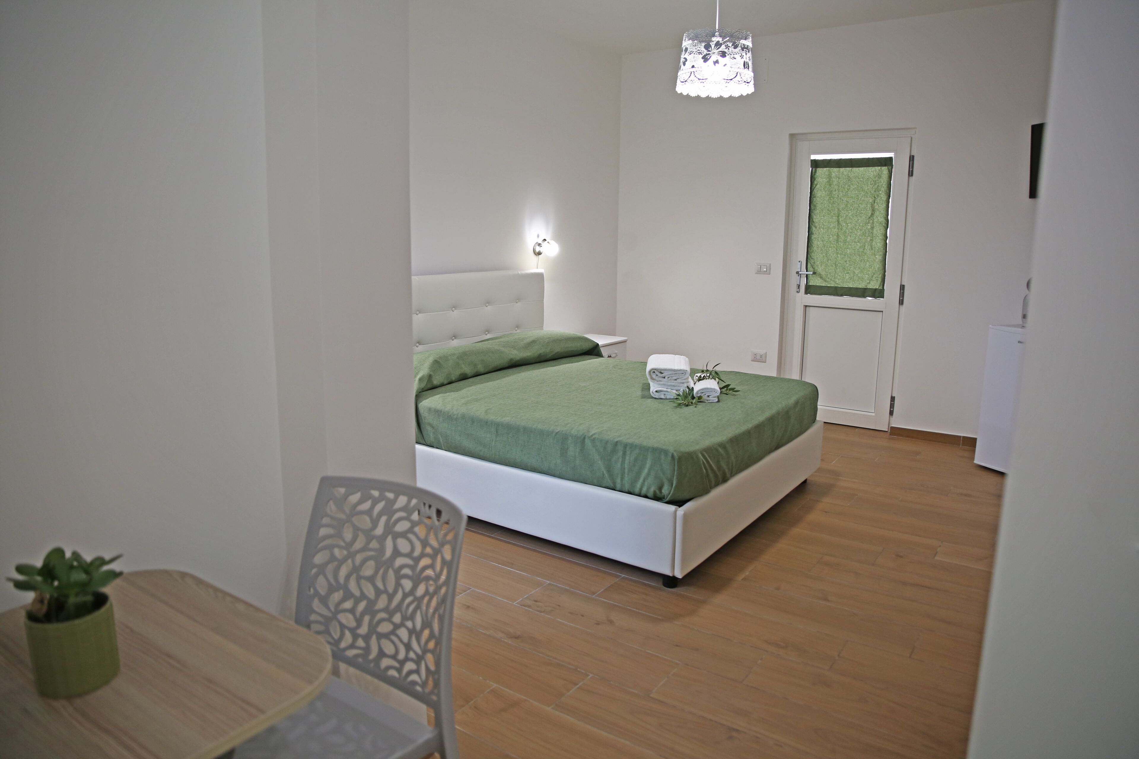 A bedroom with a bed, bedside table, chair, and a small table with a plant.