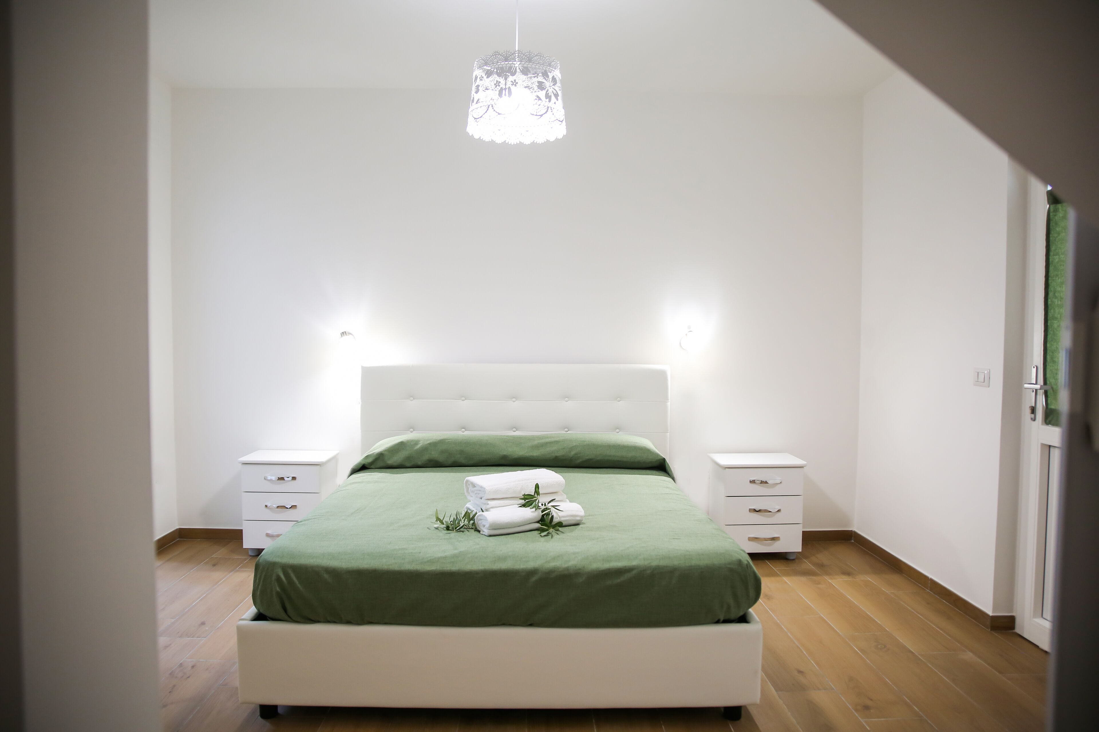 A bedroom with a bed, two bedside tables, a hanging light fixture, and a green bedspread.
