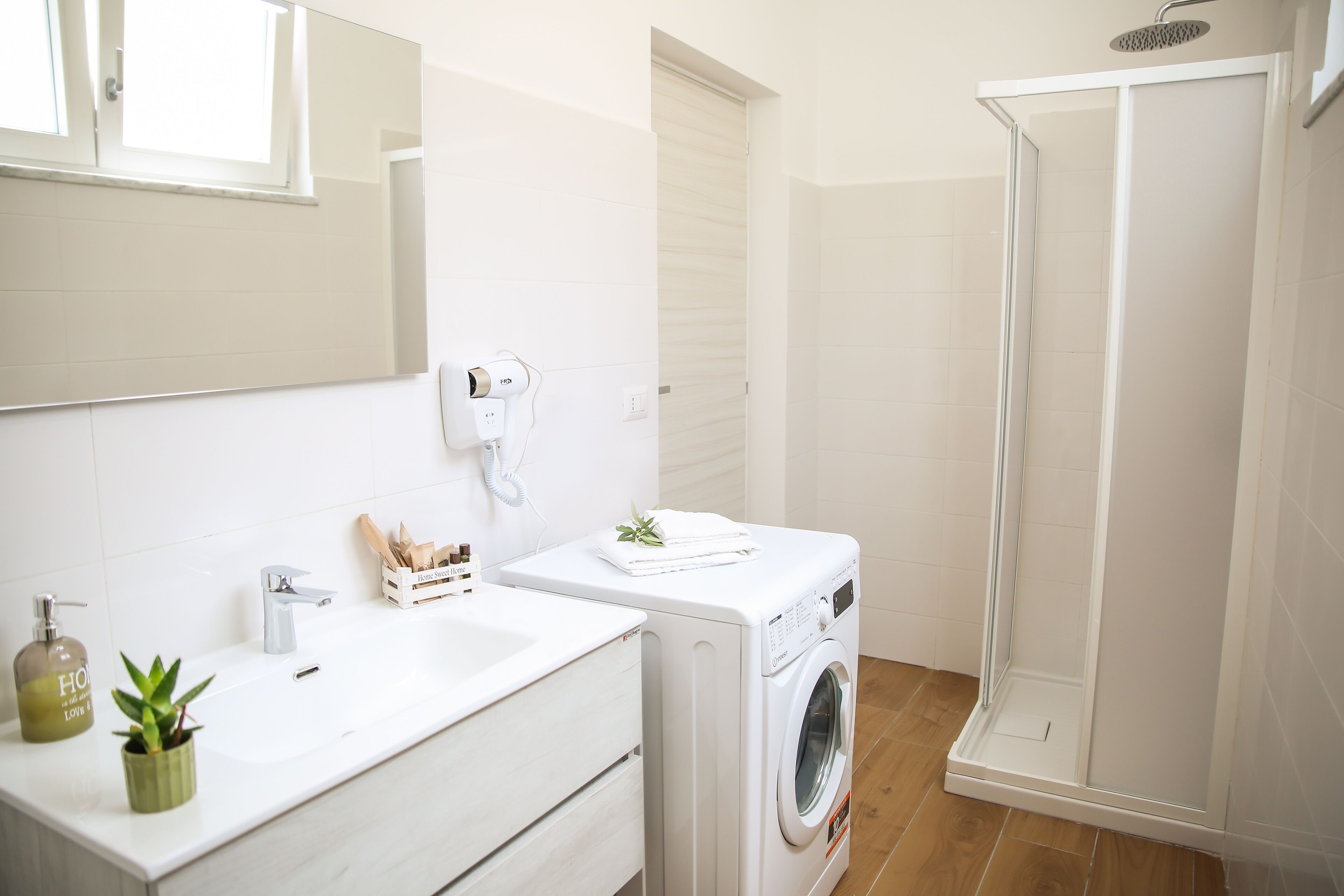 A modern bathroom with a white sink, a washing machine, and a glass-enclosed shower.