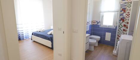 A hotel room with a bed, a bathroom with a toilet and sink, and a shower area.