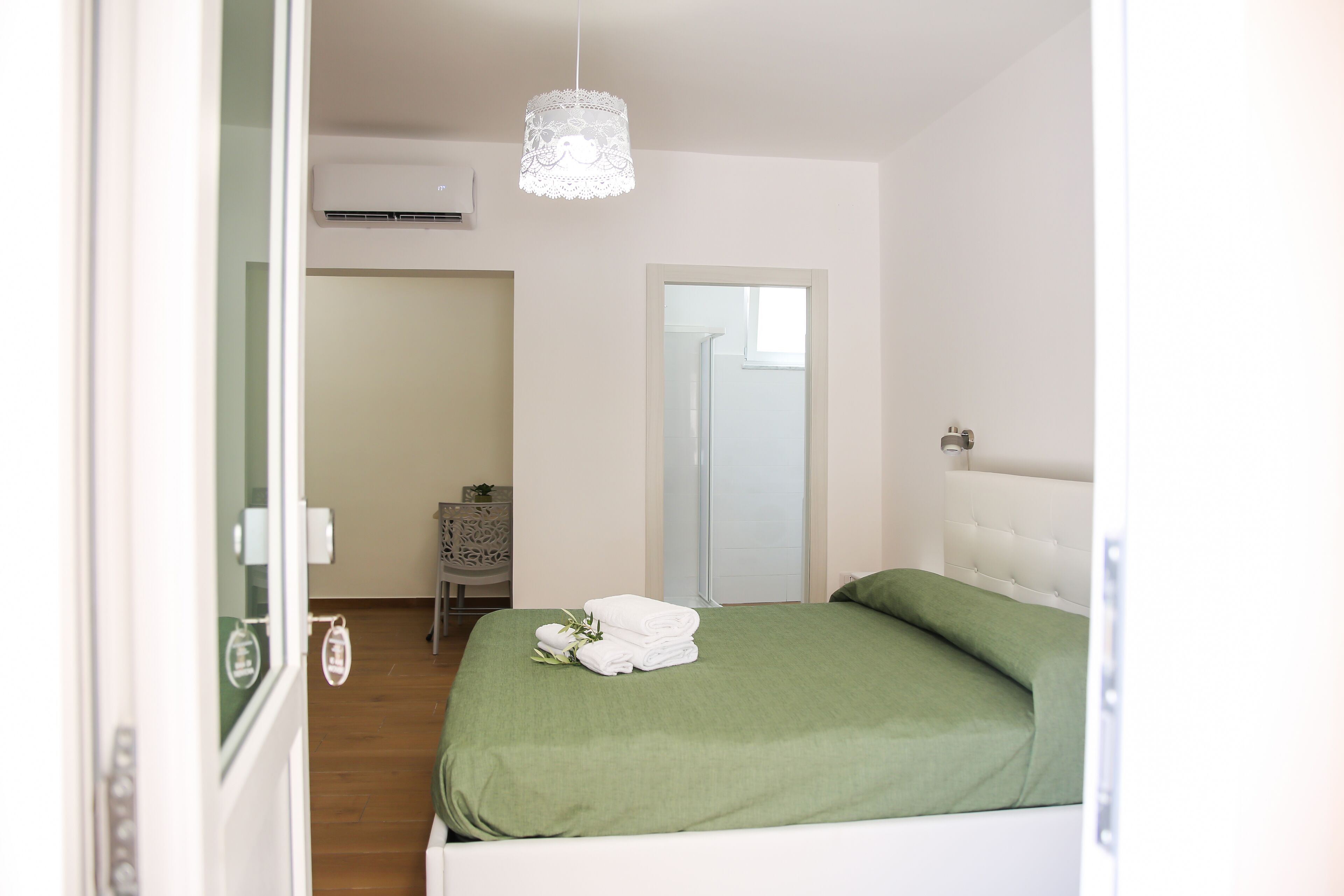 Een slaapkamer met een bed, een hanglamp, een spiegel en een deur naar een andere kamer.