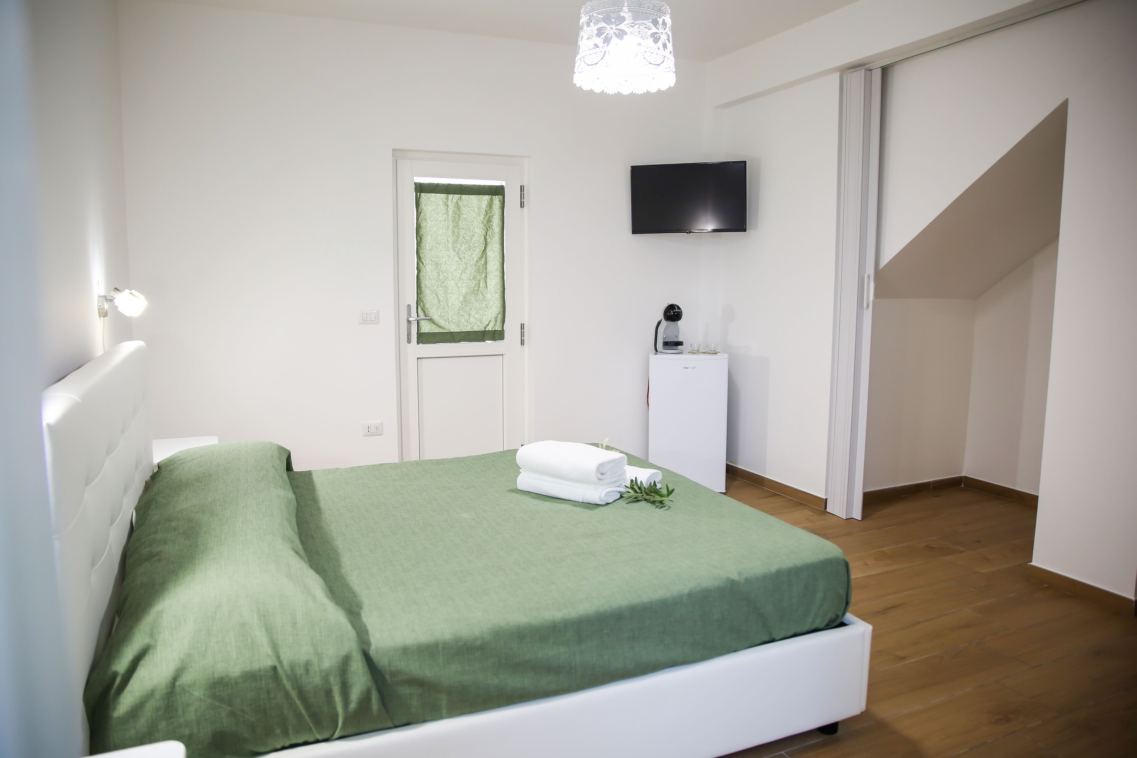 A bedroom with a bed, a TV, a small cabinet, and a door with a green curtain.