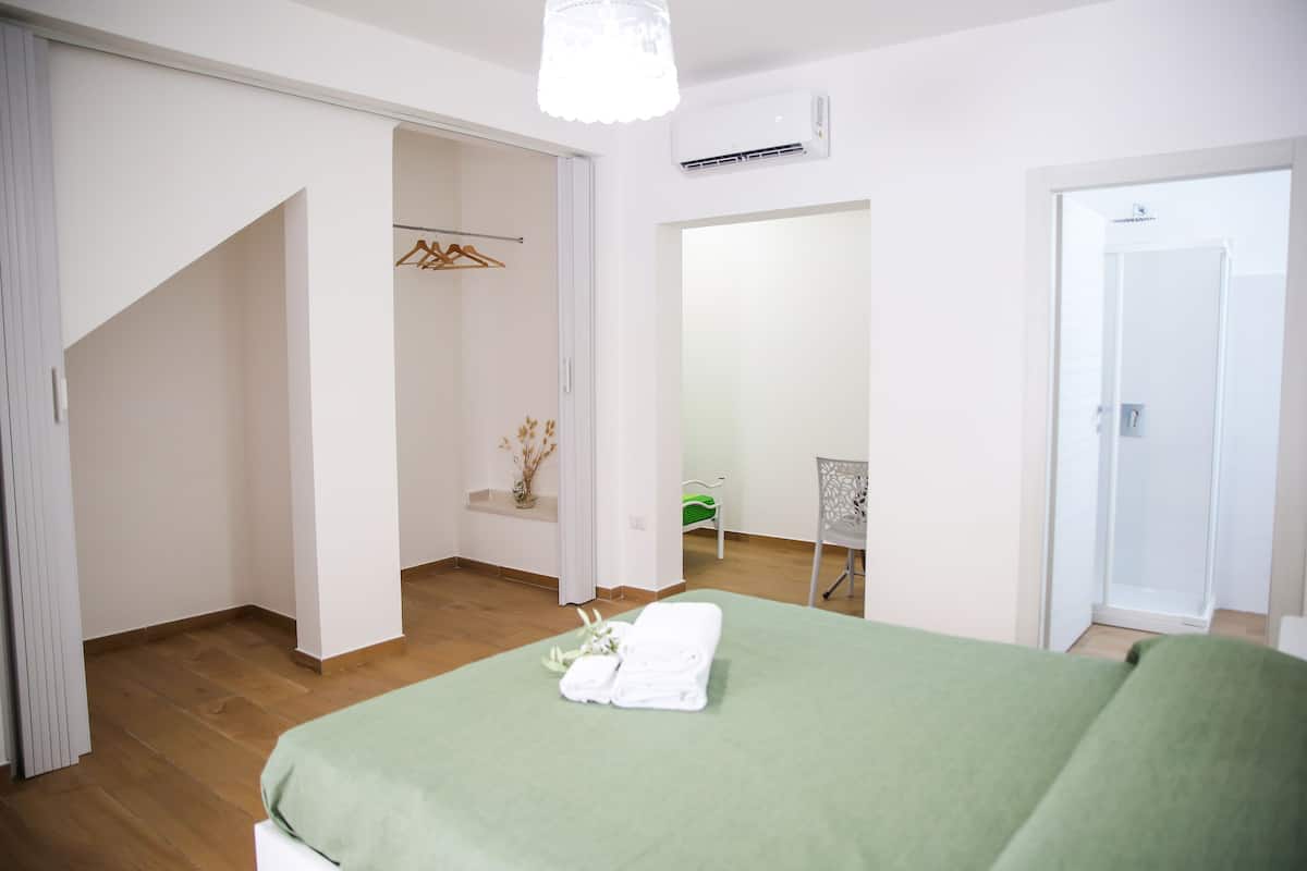 Ein Schlafzimmer mit grüner Bettdecke, Holzboden, weißem Kleiderschrank und Spiegel.