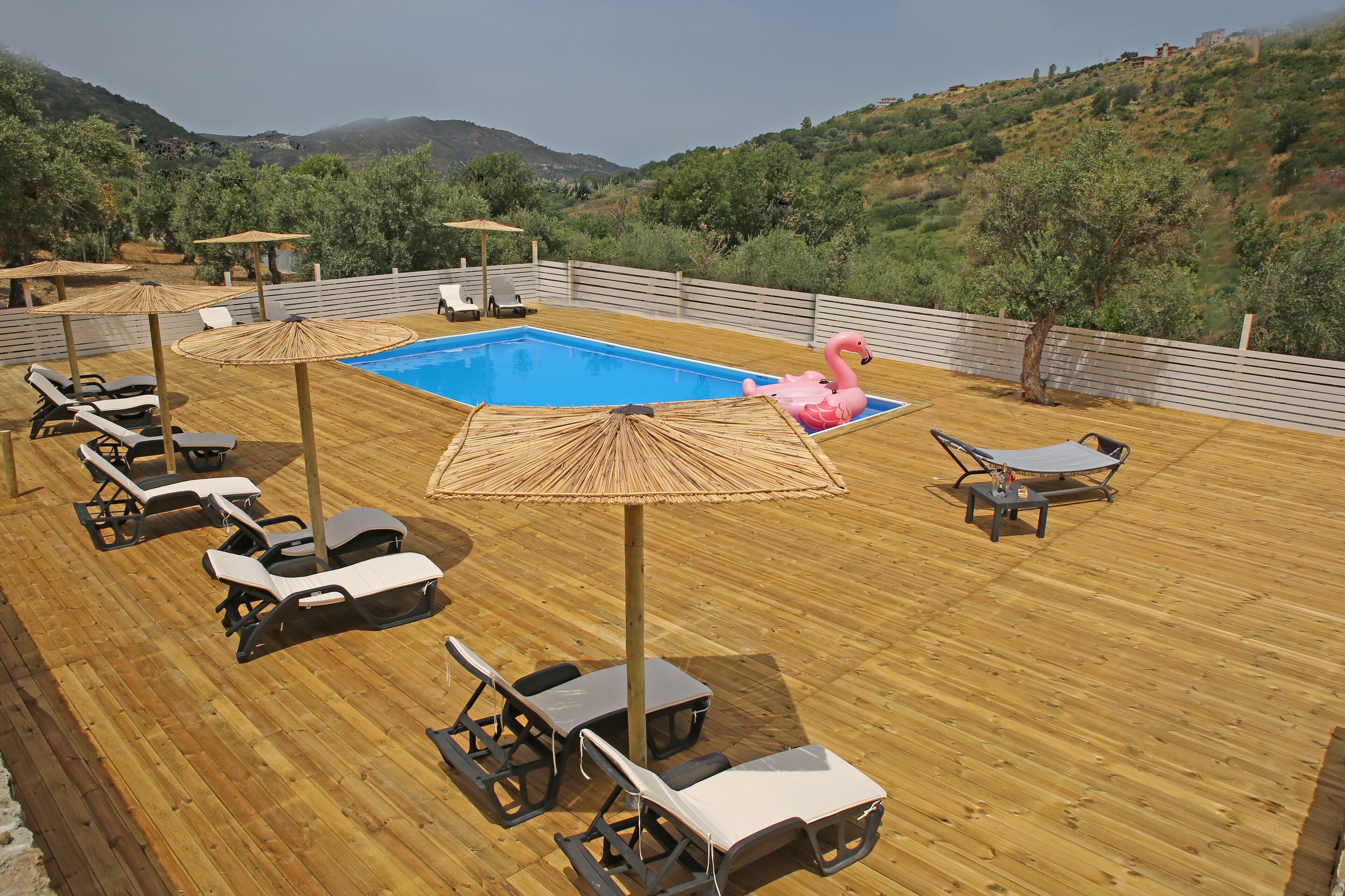A wooden deck with a pool, lounge chairs, and umbrellas.