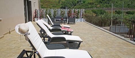 Une terrasse avec des chaises longues, une table et des chaises.