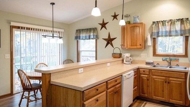 A kitchen with wooden cabinets, a central island, a dishwasher, and a dining area with chairs. - Goshorn Lake Resort Cottage #2 (Saugatuck)