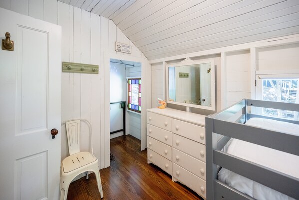 A white room with a bunk bed, a dresser, a chair, and a door.