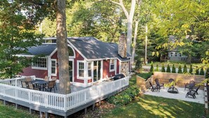 Ein Haus mit überdachter Terrasse, einer Holzterrasse und einem Hinterhof mit Grillplatz.