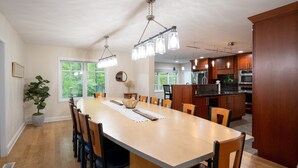 A spacious dining area with a long table, chairs, and pendant lighting.