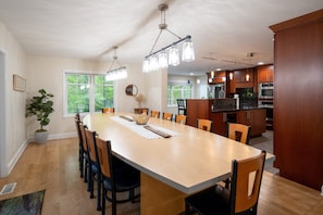 A spacious dining area with a long table, chairs, and pendant lighting.