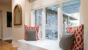 A room with a built-in bench by a window, a mirror on the wall, and a stone wall visible through the window.