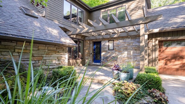 A two-story house with a stone facade, a blue door, and a covered patio area.