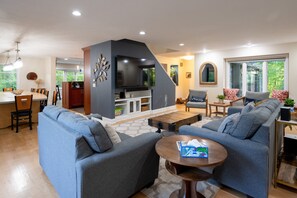 A modern living room with a fireplace, sofas, a dining area, and a kitchen.