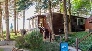 A wooden cabin with a staircase leading to the entrance, surrounded by trees and greenery. - Lakefront Cottage | Private Beach + Sunset Views (Holland)
