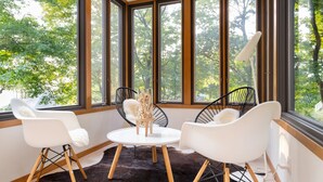 Une pièce moderne dotée de grandes fenêtres, d’une table ronde et de deux chaises blanches aux pieds en bois.