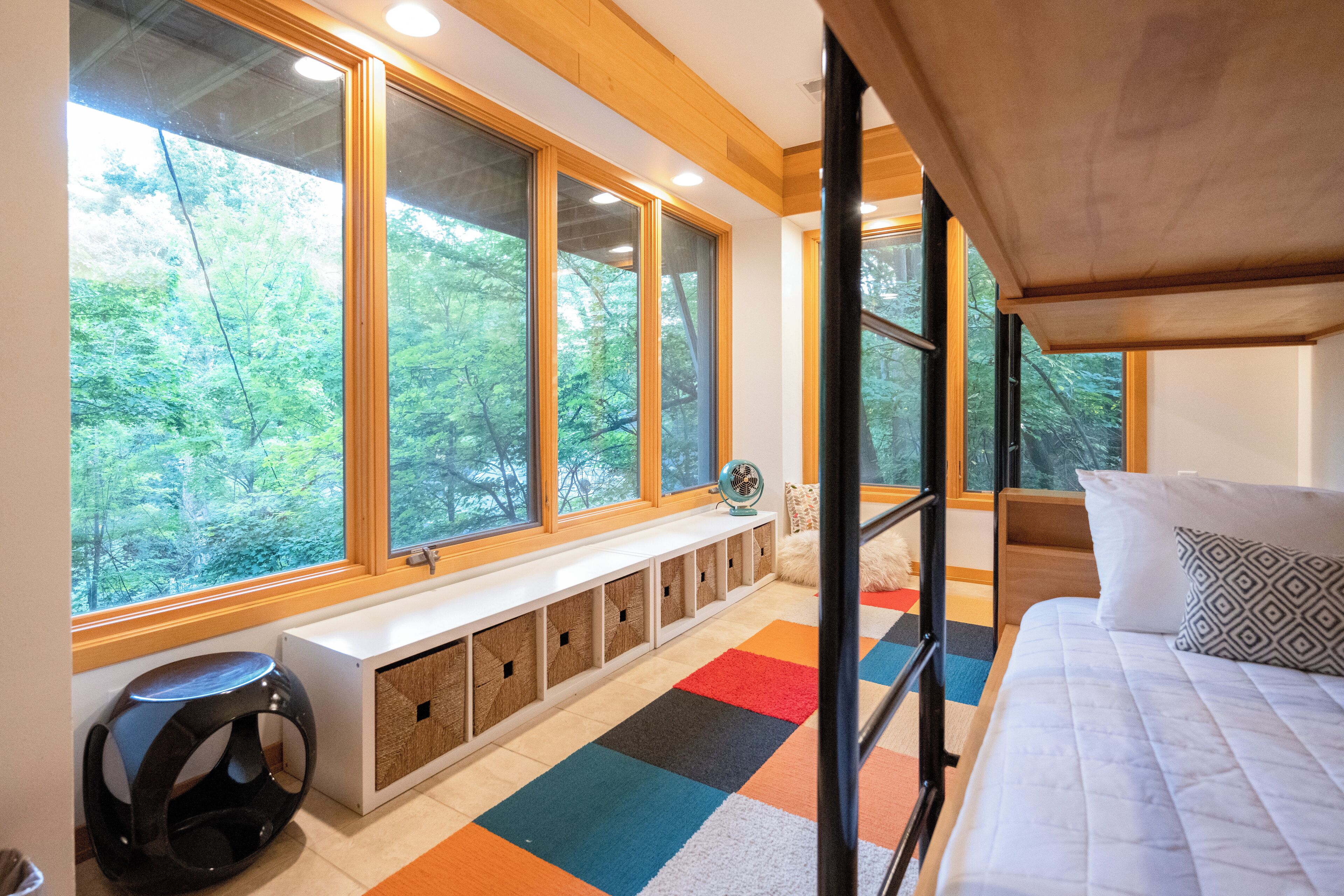 A bedroom with a large window, a bed, a bench with storage, and a view of the forest.