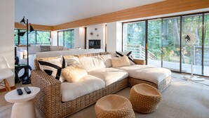 Un salon moderne doté d’un grand canapé d’angle, de poufs en osier, d’une table basse blanche et d’une grande fenêtre donnant sur l’extérieur.